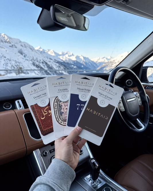 The Grand Tour Bundle: Buy 3 Get 1 Free: hand holding the Tawakkul, Eau de Lavande, Lucky 777 and Habitair Classic HabitAir retail packs in a car