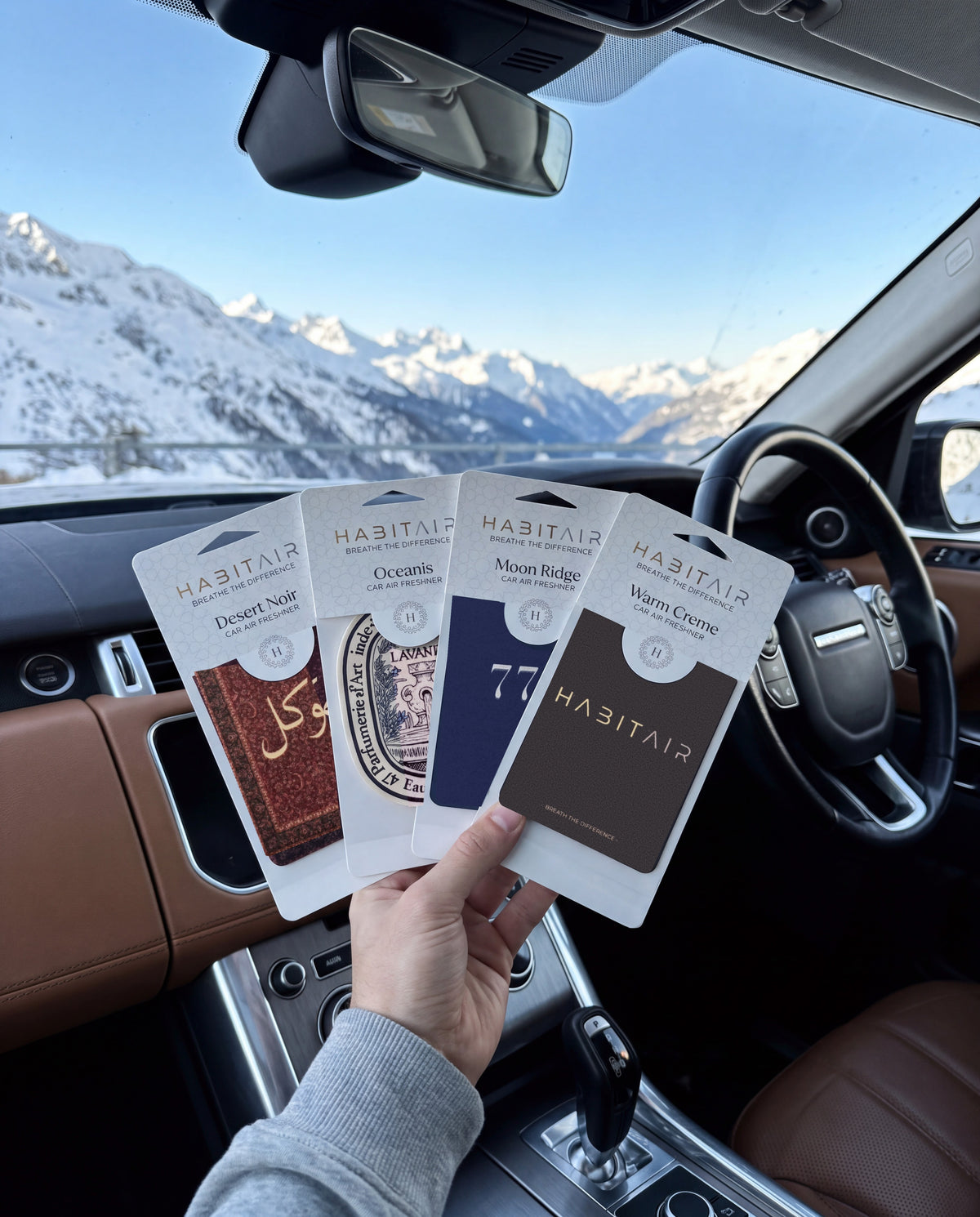 The Grand Tour Bundle: Buy 3 Get 1 Free: hand holding the Tawakkul, Eau de Lavande, Lucky 777 and Habitair Classic HabitAir retail packs in a car